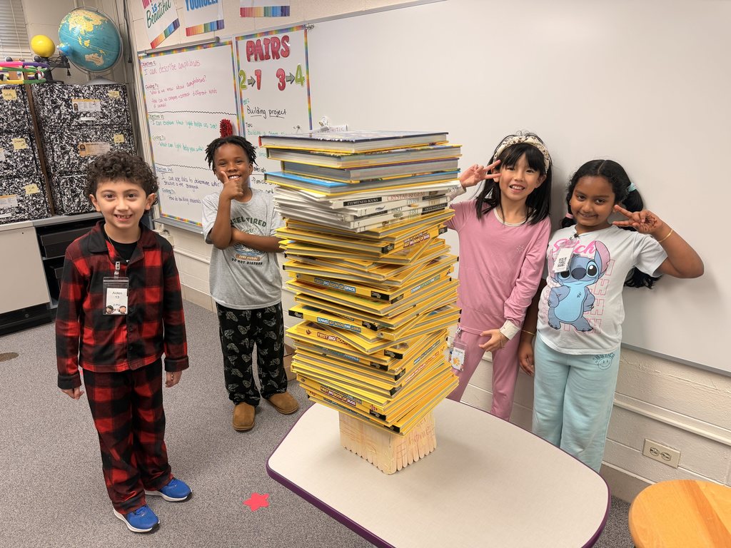 Four students pose together and smile with their project holding a large stack of books