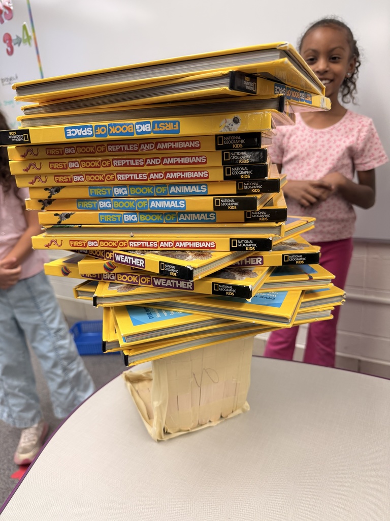 Students smile with their project holding a large stack of books