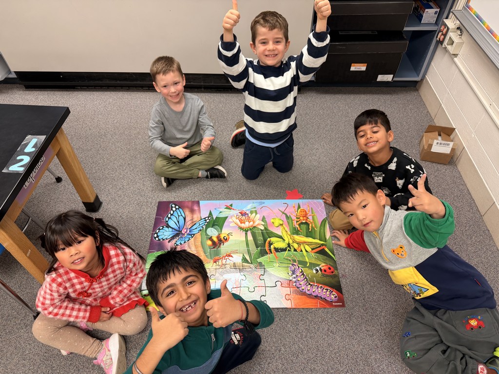 Students sit on the floor with an animal puzzle and smile at the camera