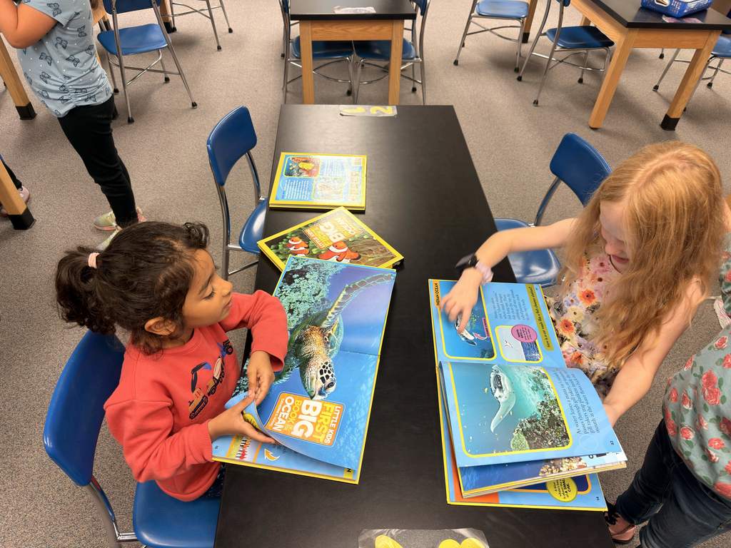 Two students sit at a desk and read books about animals