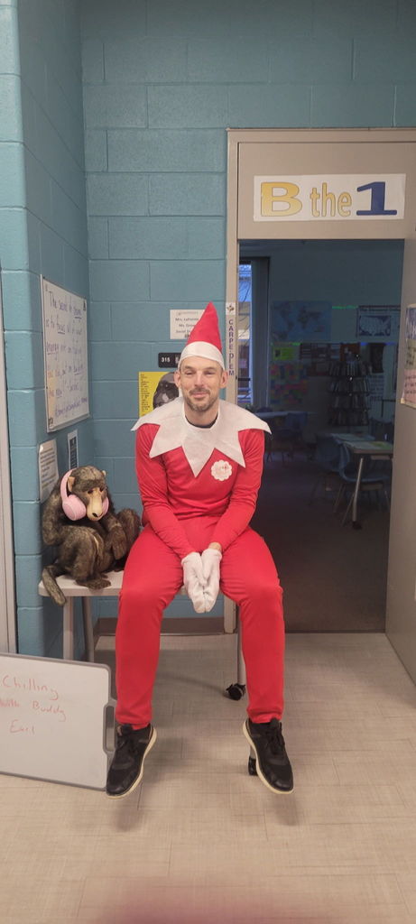 Man dressed as Elf on the shelf sitting on a table with a monkey with headphones