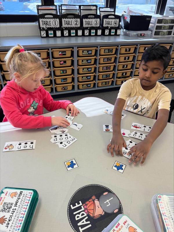Kindergarteners sit at a table and play a learning game together