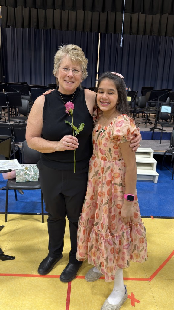 Mrs. Casey smiling at the camera with a flower in her hand and a student