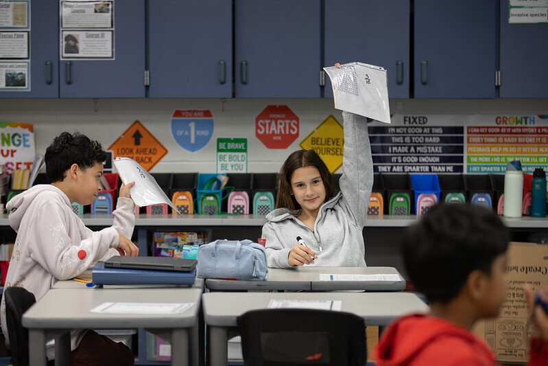 Students raise their papers with their math answers written