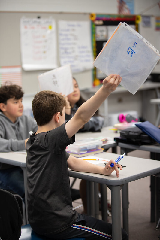 Students raise their papers with their math answers written