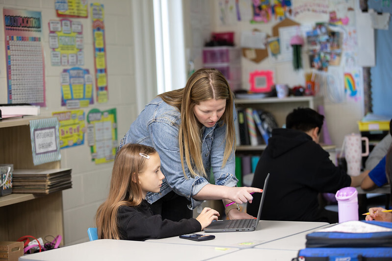 A teacher works with a student, pointing to the student's laptop