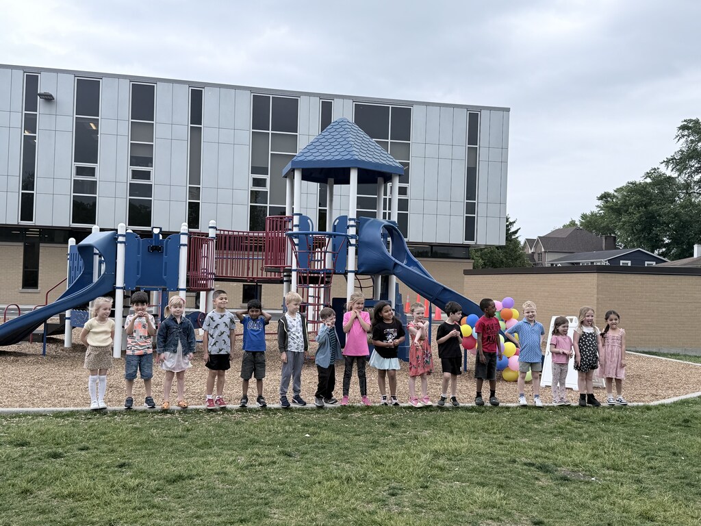 New first graders pose in front of the slide on the playground after "sliding into first grade"