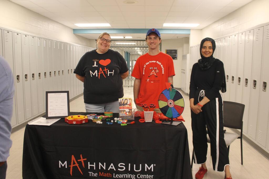 Three staff members pose and smile behind a Mathnasium table