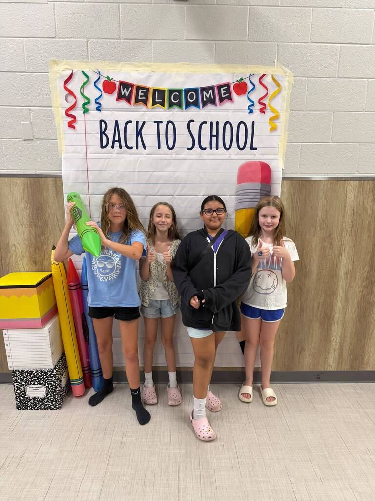 Four students pose in front of a Back to School banner
