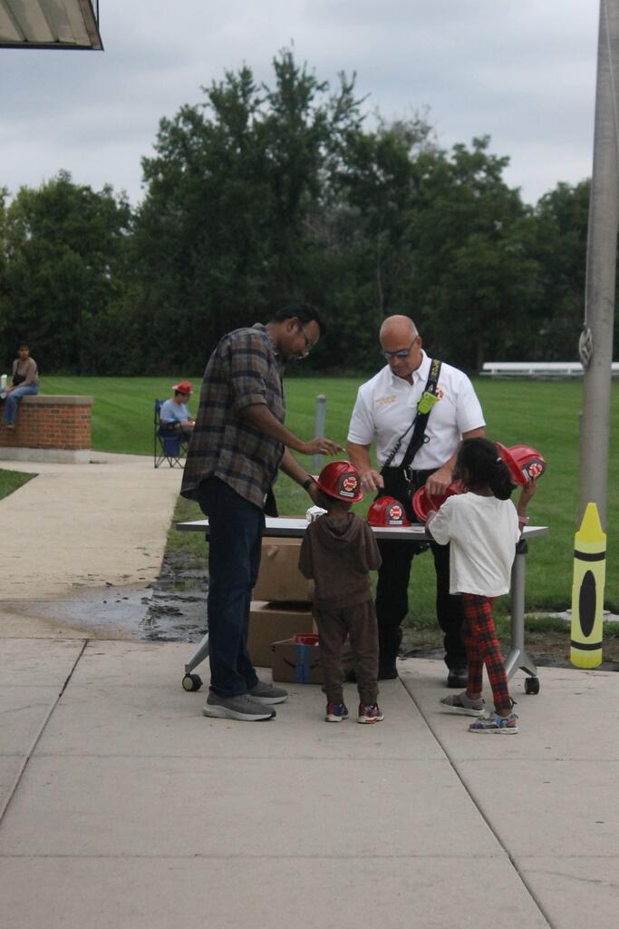 Students interact with a firefighter and wear firefighter helmets