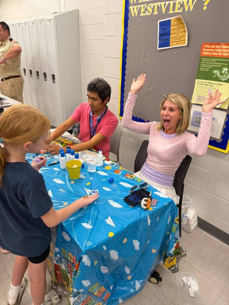A staff member interacts with a student at a table and has an excited expression