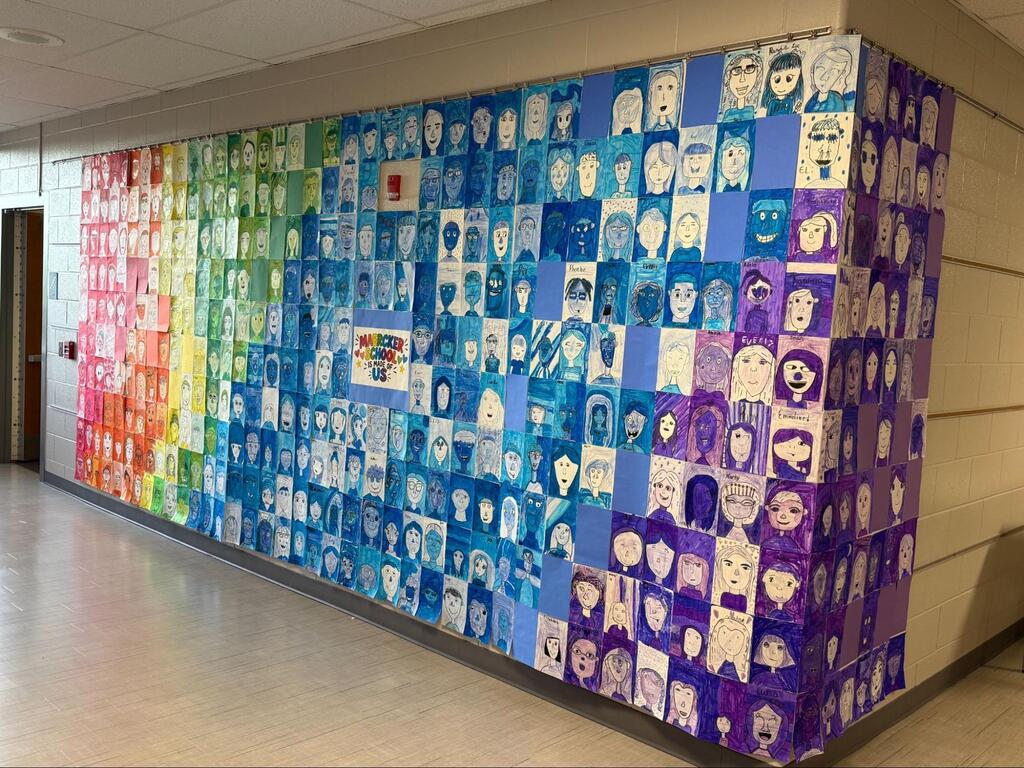 collaborative art project on wall filled with rainbow colored self-portraits