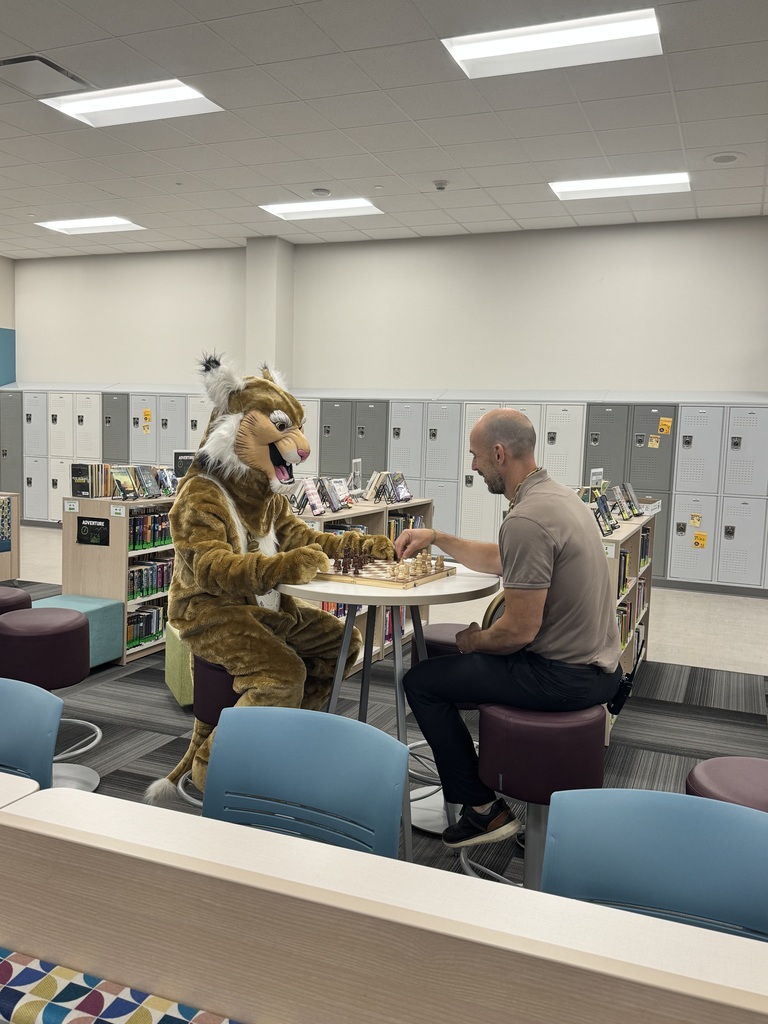 wildcat mascot and principal playing chess in the library