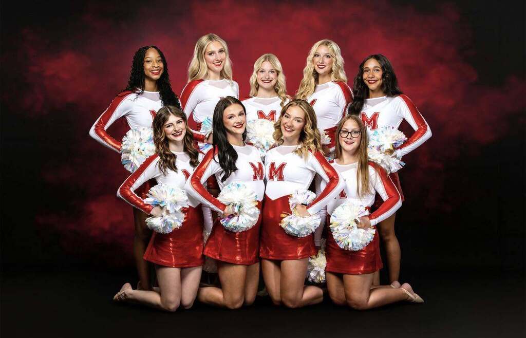 Cheerleaders in red and white uniforms with pom-poms pose for a photo against a red background.