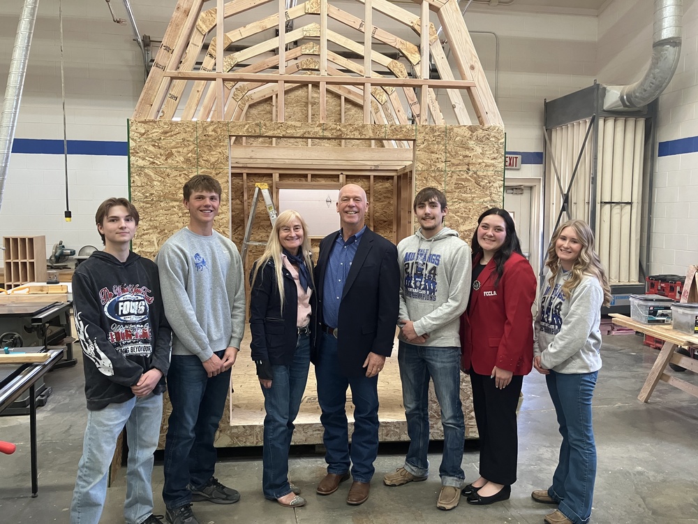students with the governor in front of a shed