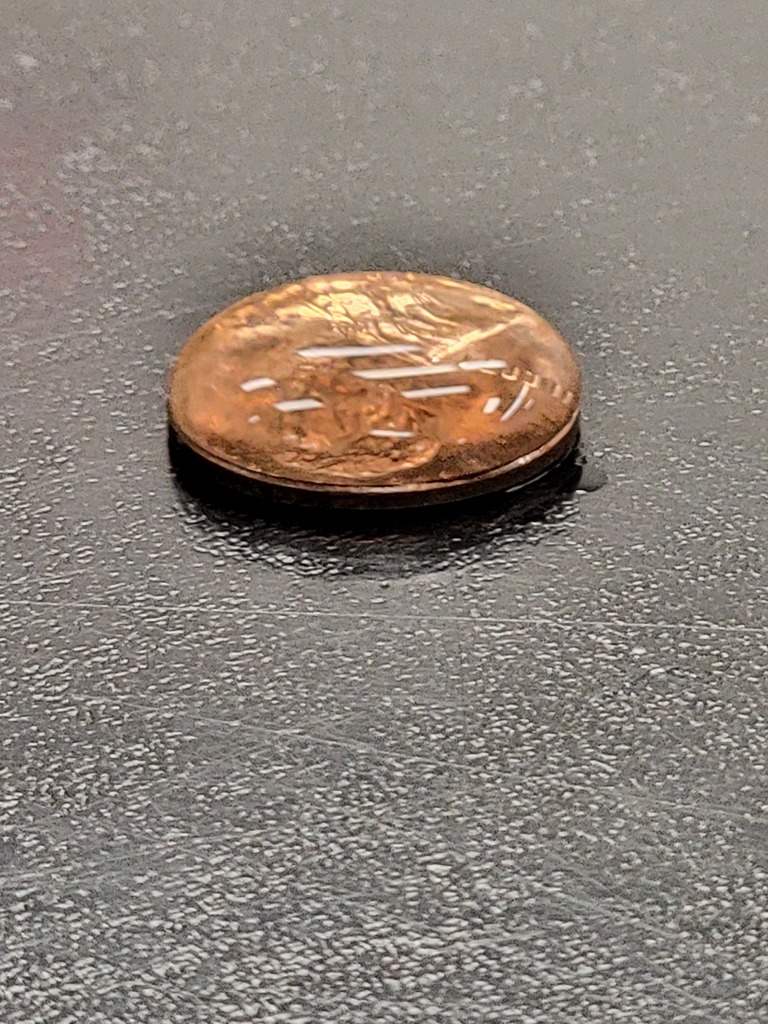 Penny with 50 drops of water stacked on top.