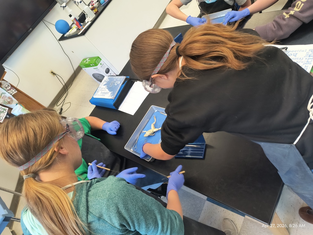Three students dissecting a frog, though one student's face is obstructed.