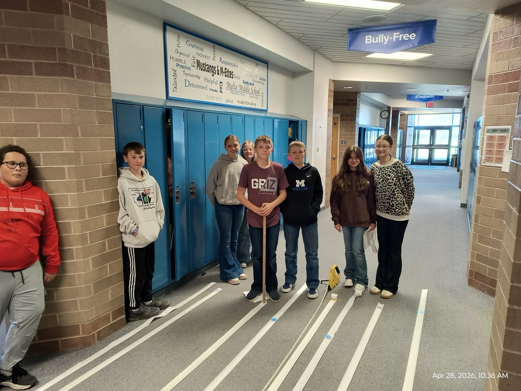 A group of students standing beside 100 ft long strips of receipt tape marked with scale images of the planets of the solar system.