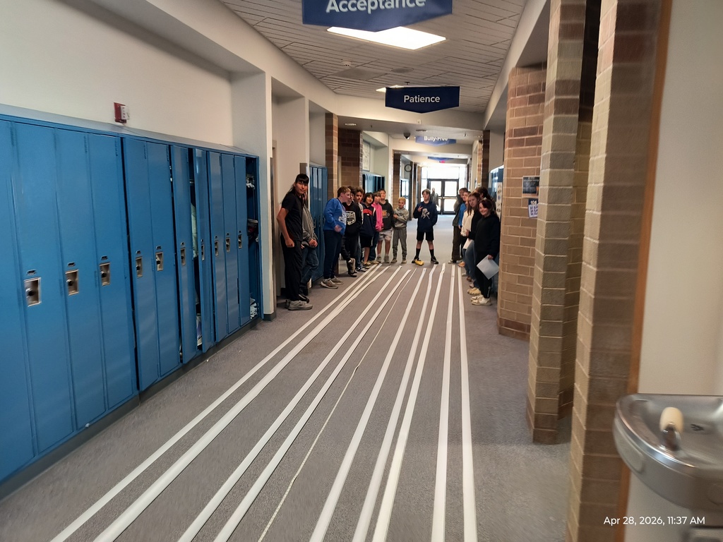 A group of students standing beside 100 ft long strips of receipt tape marked with scale images of the planets of the solar system.