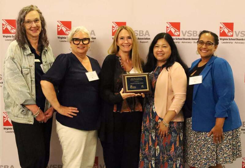 Members of the school board holding a plaque infront of a VSBA background