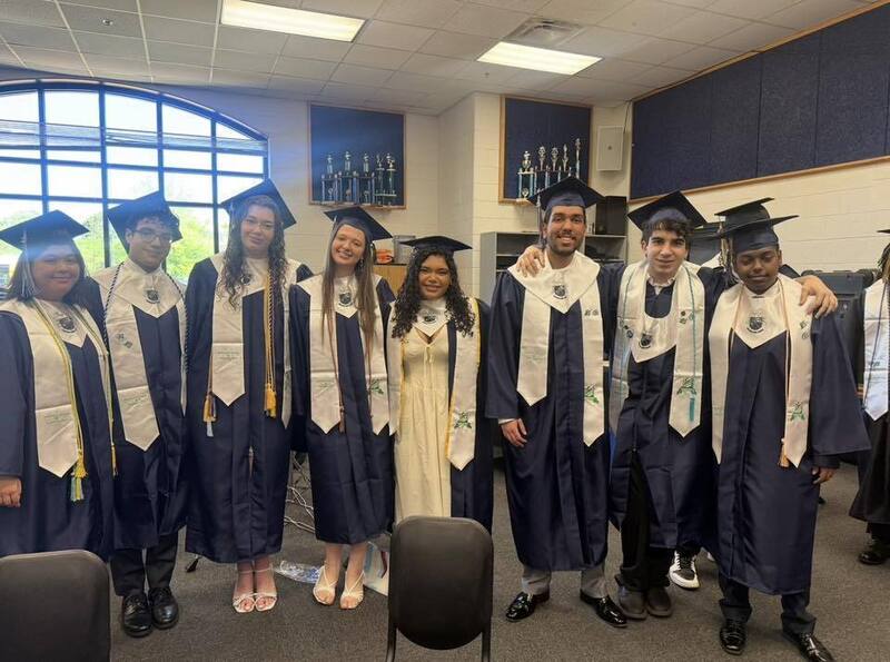 Group of students in navy cap and gowns and white sashes.