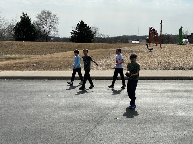 5th graders playing football on blacktop playground woodchips trees in background 
