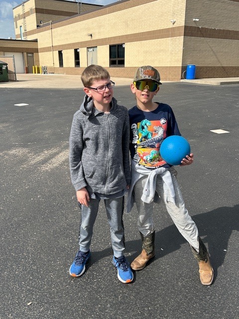 5th graders smiling for a picture school in the background 