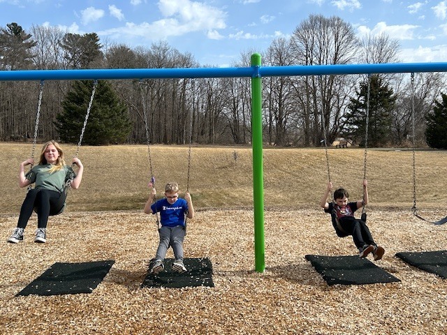 5th graders  on the swing set trees hill and grass in the background 