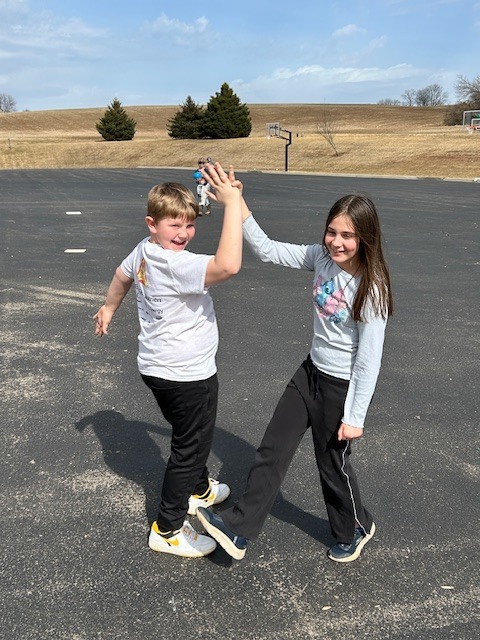 5th graders high fiving outside trees and grass in background along with basketball hoops 