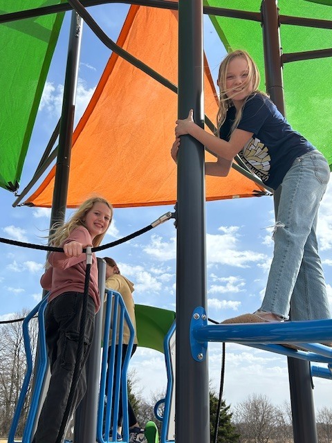 5th graders on the playground orange and green flags on the top of playground trees in the background 