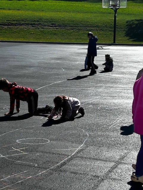 Kindergarten buddies with 3rd graders outside playing with chalk on the blacktop