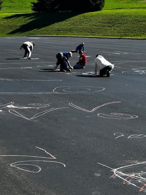 Kindergarten buddies with 3rd graders outside playing with chalk on the blacktop