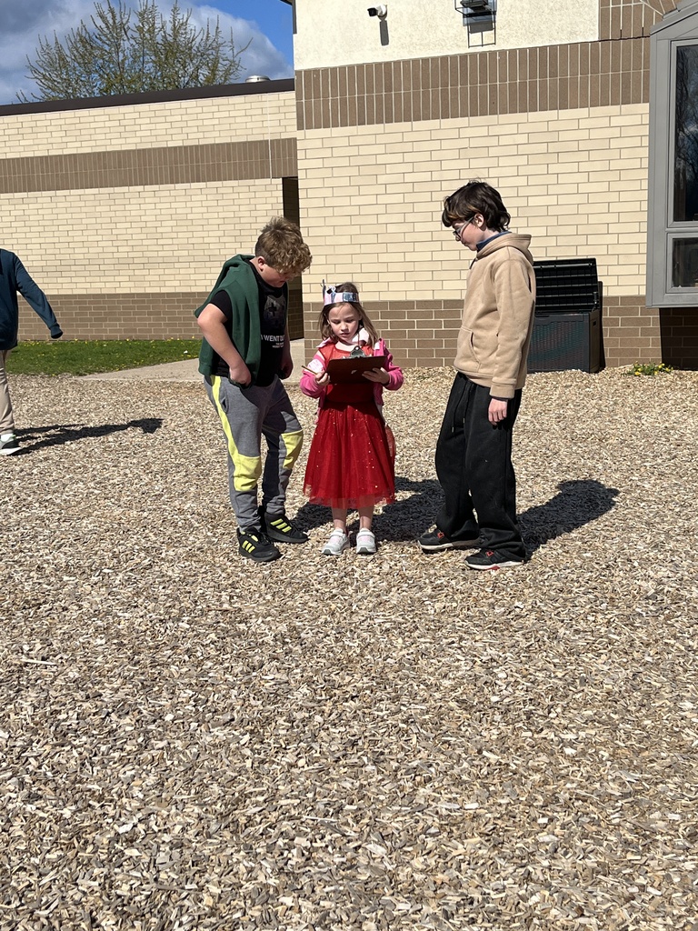 4th grade and kindergarten students outside participating in a scavenger hunt playground in the background