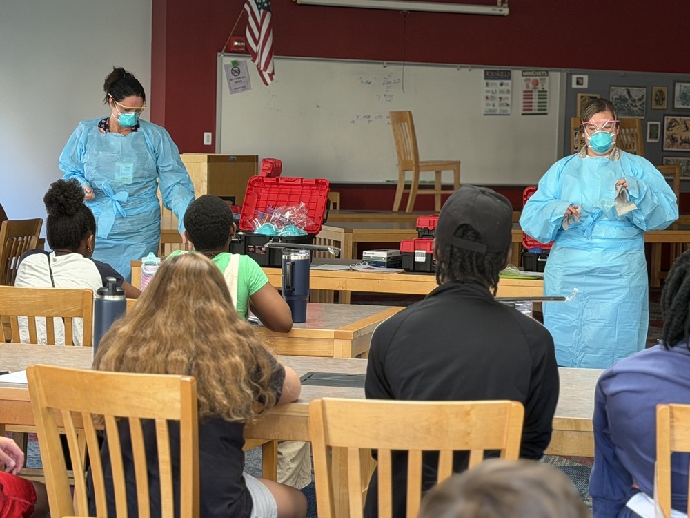 Nurses in PPE gear speak with 21c students