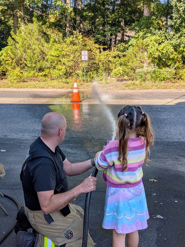 A firefighter supervises MTES students using a fire hose
