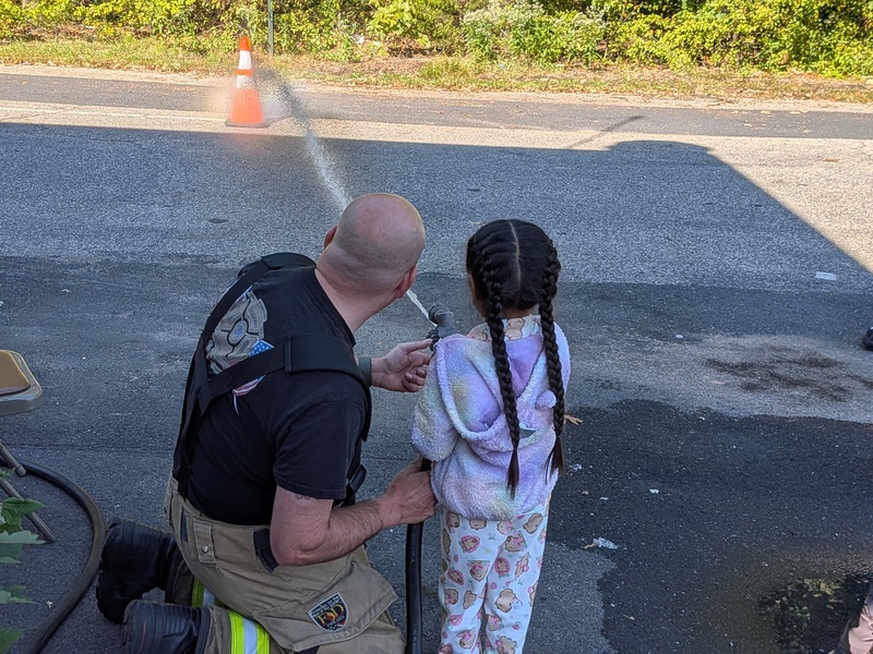 A firefighter supervises MTES students using a fire hose
