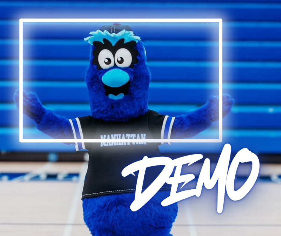 A blue mascot wearing a black shirt with white trim stands on a court with blue bleachers.