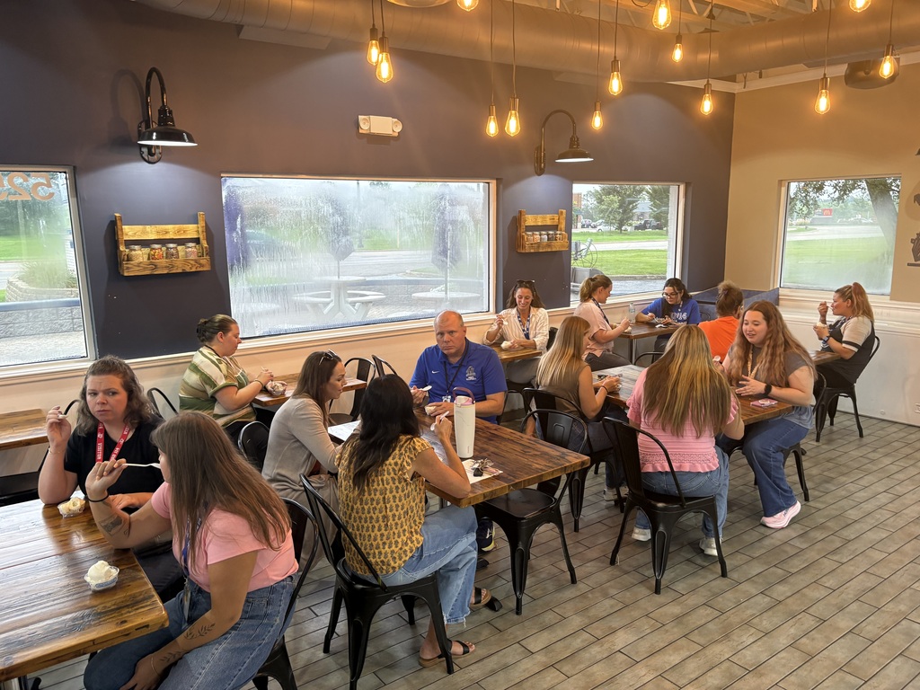 People sit at tables in a dining area of a restaurant with brick flooring. Large windows are on the walls.
