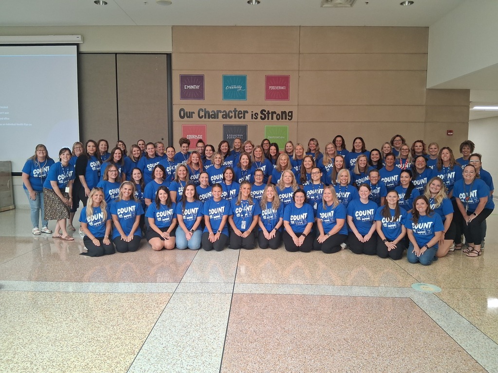A group of individuals in blue shirts and jeans, posing for a photo in a room with a large mural.