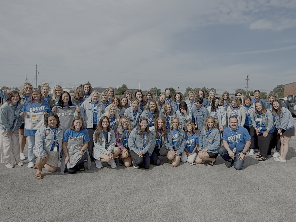 A group of individuals in matching blue shirts stands together in a parking lot. They are posing for a photo.
