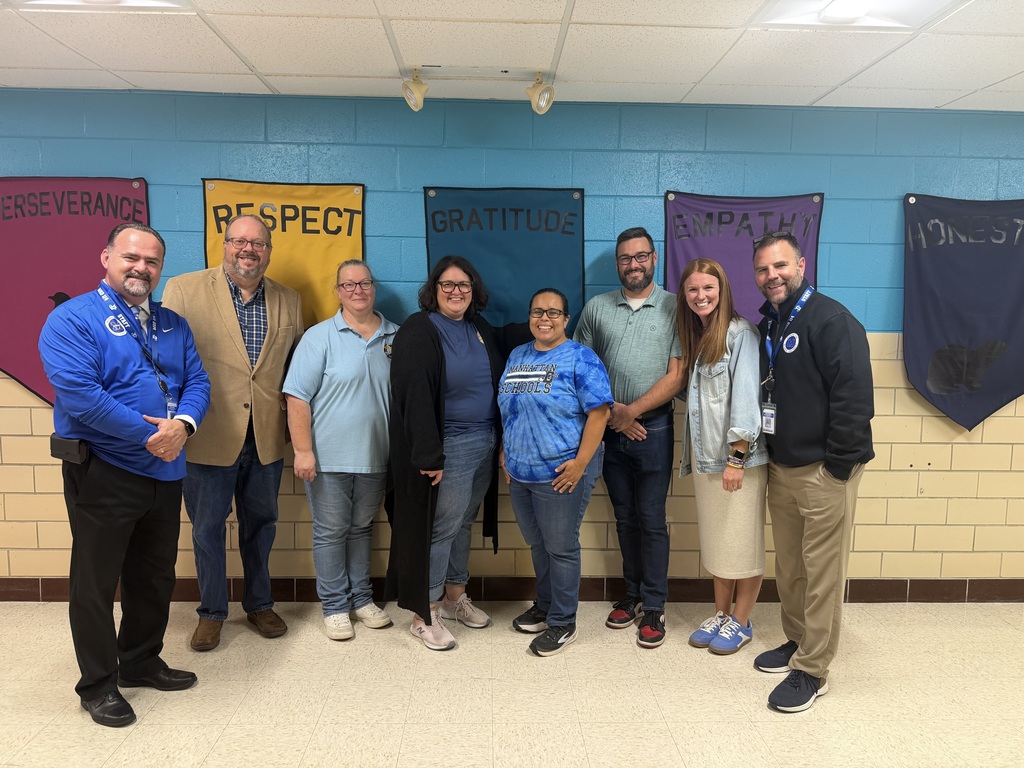Seven people stand in a row in front of a blue wall with banners reading "Respect," "Gratitude," and "Courage."