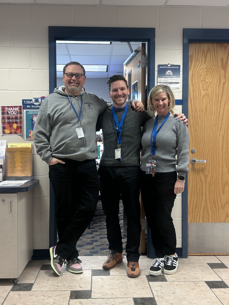 Three smiling school administrators stand arm-in-arm in a doorway at a school, unintentionally dressed alike in gray tops, black pants, and blue lanyards with ID badges. 