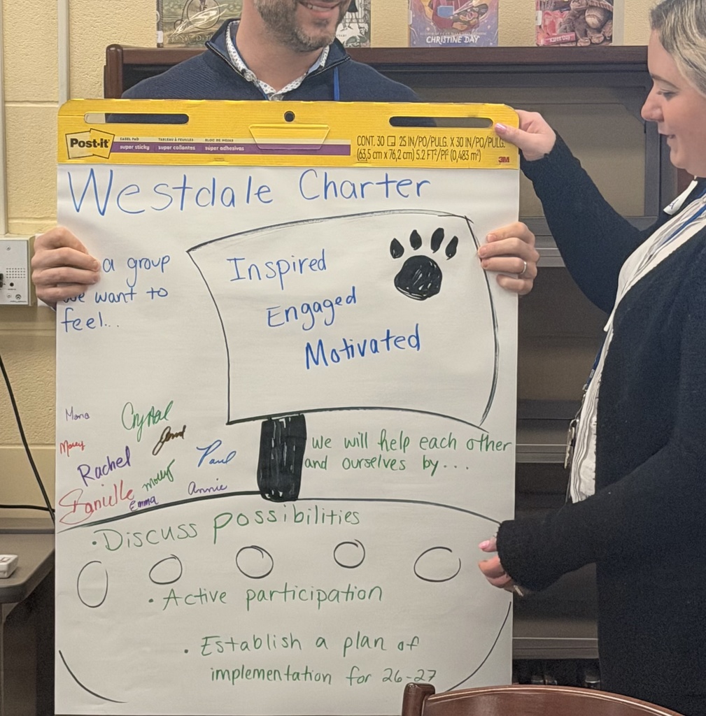 Two staff members hold a large Post-it easel pad titled "Westdale Charter" featuring brainstorming notes from a collaborative session. The paper includes a hand-drawn paw print with the words "Inspired, Engaged, Motivated," a list of team names, and goals such as "Discuss possibilities," "Active participation," and "Establish a plan of implementation for 26-27."