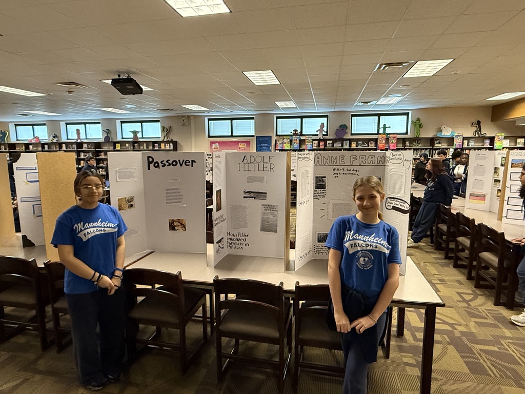 Two students in blue t-shirts standing proudly in front of display boards about research for History Fair