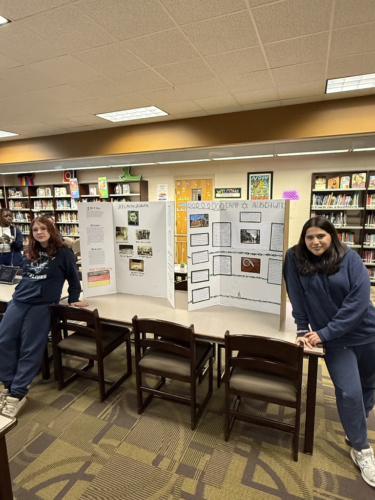 Two students in blue hoodies and blue slacks standing proudly in front of display boards about research for History Fair