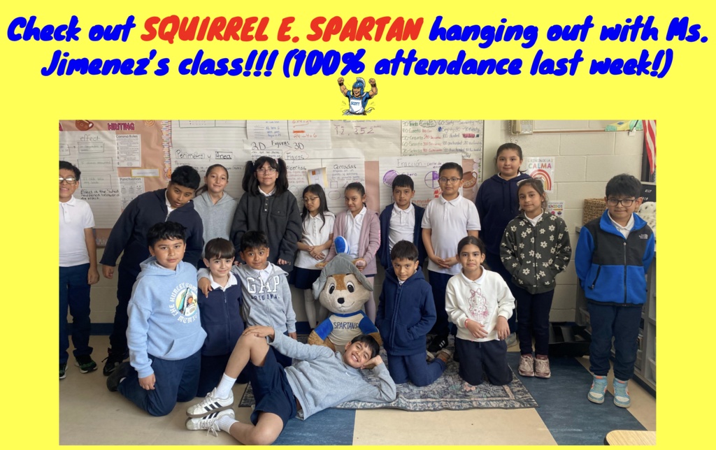 A classroom photo of Ms. Jimenez’s students smiling and posing together to celebrate 100% attendance. In the center, the students are gathered around Squirrel E. Spartan, a large stuffed squirrel mascot wearing a blue and white Spartan helmet and jersey. One student is playfully reclining on the floor in front of the group. The background features educational posters about math and writing.