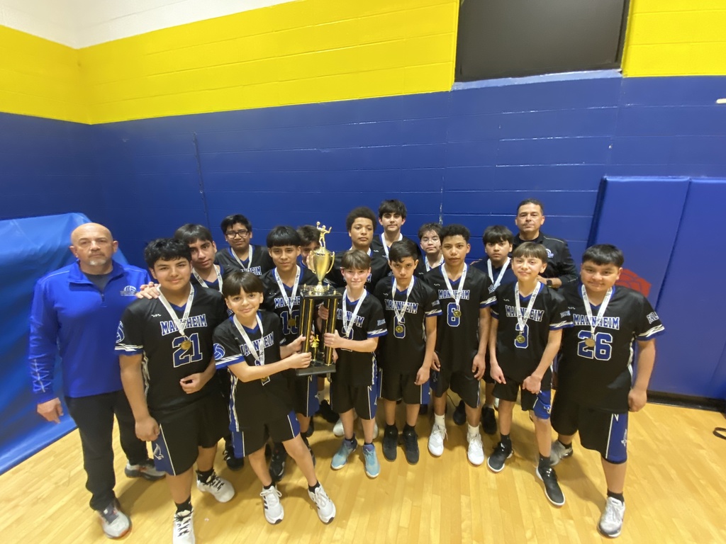 Boys volleyball team standing together on a gym court, smiling and celebrating as they hold up a championship trophy, with teammates gathered closely around and a sense of excitement and accomplishment visible on their faces.