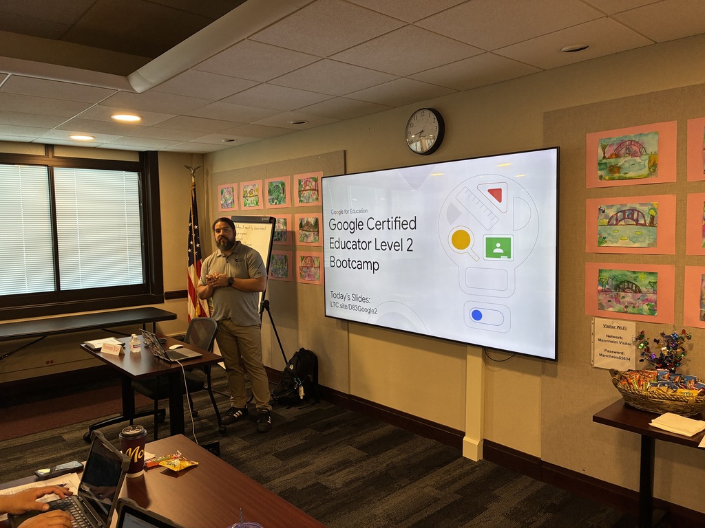 A presenter stands at the front of a training room next to a large digital screen displaying a slide that reads, "Google Certified Educator Level 2 Bootcamp" with a link to today's slides.