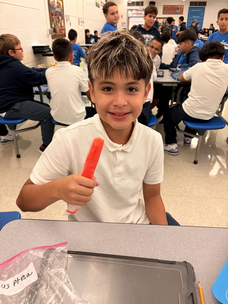 student in white polo smiling and holding a popsicle in a cafeteria