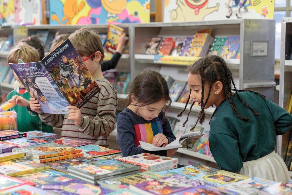 Three elementary aged children reading new book sat the Scholastic Book Fair.